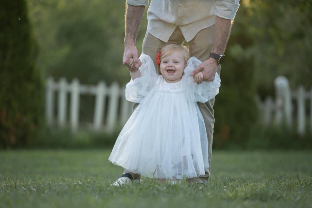 a father and a baby girl walking on a grassy field